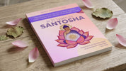 Das Buch "Santosha" in lila-rosanem Cover mit meditierendem Buddha in einem großen roten Lotus, vor dessen Herz eine Sonne erstrahlt.